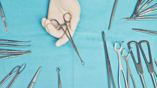 a surgeon's gloved hand holds a tool over a table of surgical tools